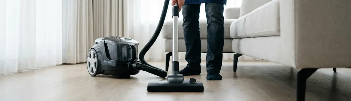 Professional house cleaner vacuuming a living room floor with a canister vacuum cleaner, Cedar Rapids, IA.