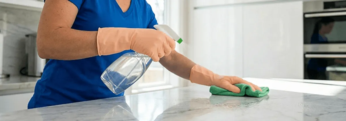 Maid service worker spraying and wiping a kitchen countertop with a microfiber cloth for sanitizing, Cedar Rapids, IA.